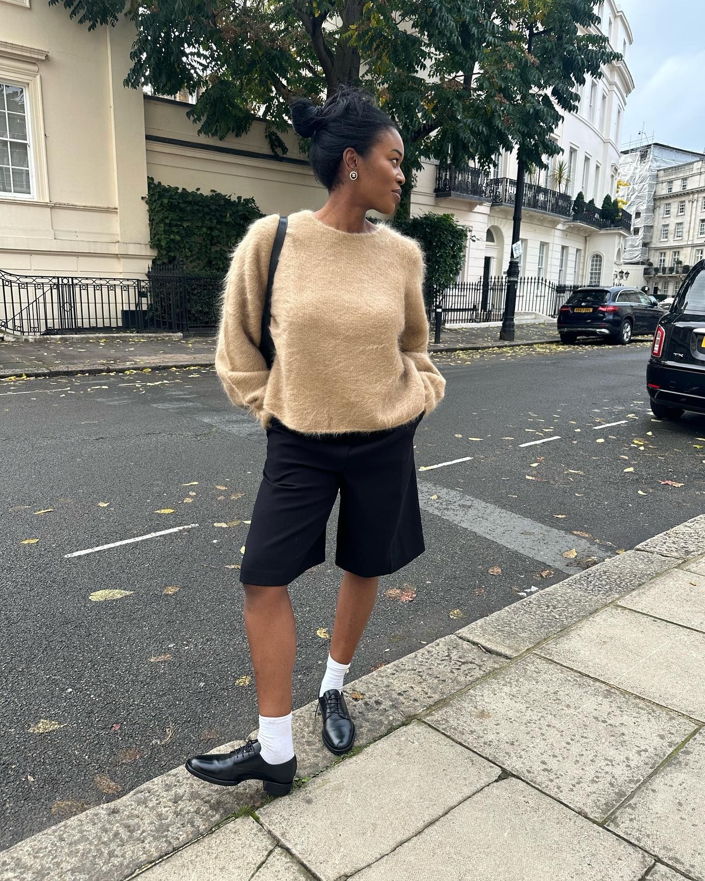 Influencer @nlmarilyn stands outside wearing Oxford shoes, long shorts and a fuzzy jumper.