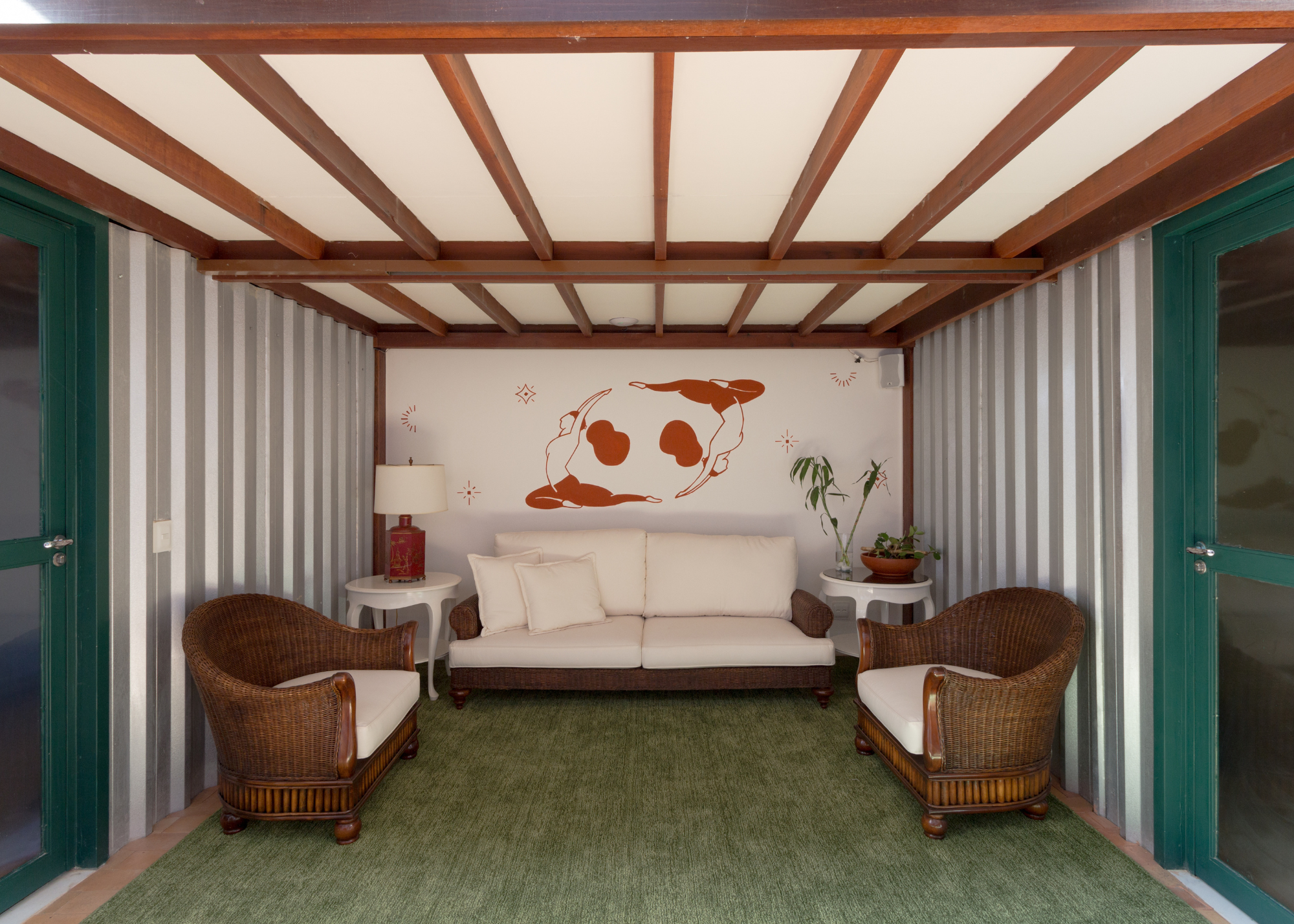 A vaulted ceiling living room with a green, earthy toned carpet and wooden chairs with white cushions