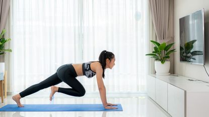 A woman doing mountain climbers on a yoga mat in her living room