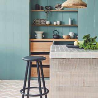 Kitchen island in a blue panelled kitchen with singular stool.