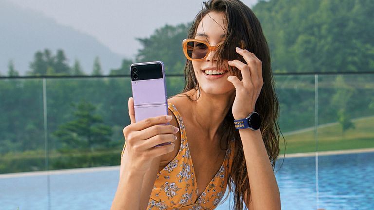 The best foldable phones hero image showing a woman in swim suite and wearing sunglasses using a Samsung Galaxy Z Flip 3 5G folding phone to take a selfie