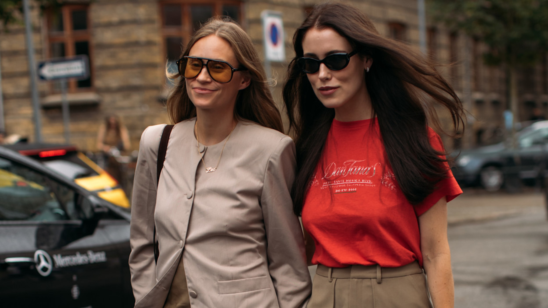 woman wearing a tan blazer and jeans next to a woma in a red tee and a brown skirt