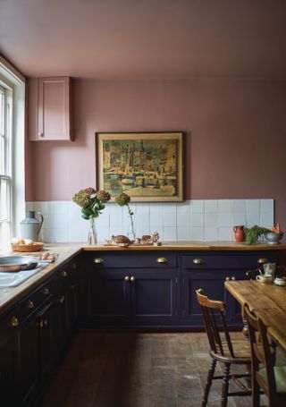 A navy blue kitchen with white tiled splashback, wood block countertops and soft muted pink walls