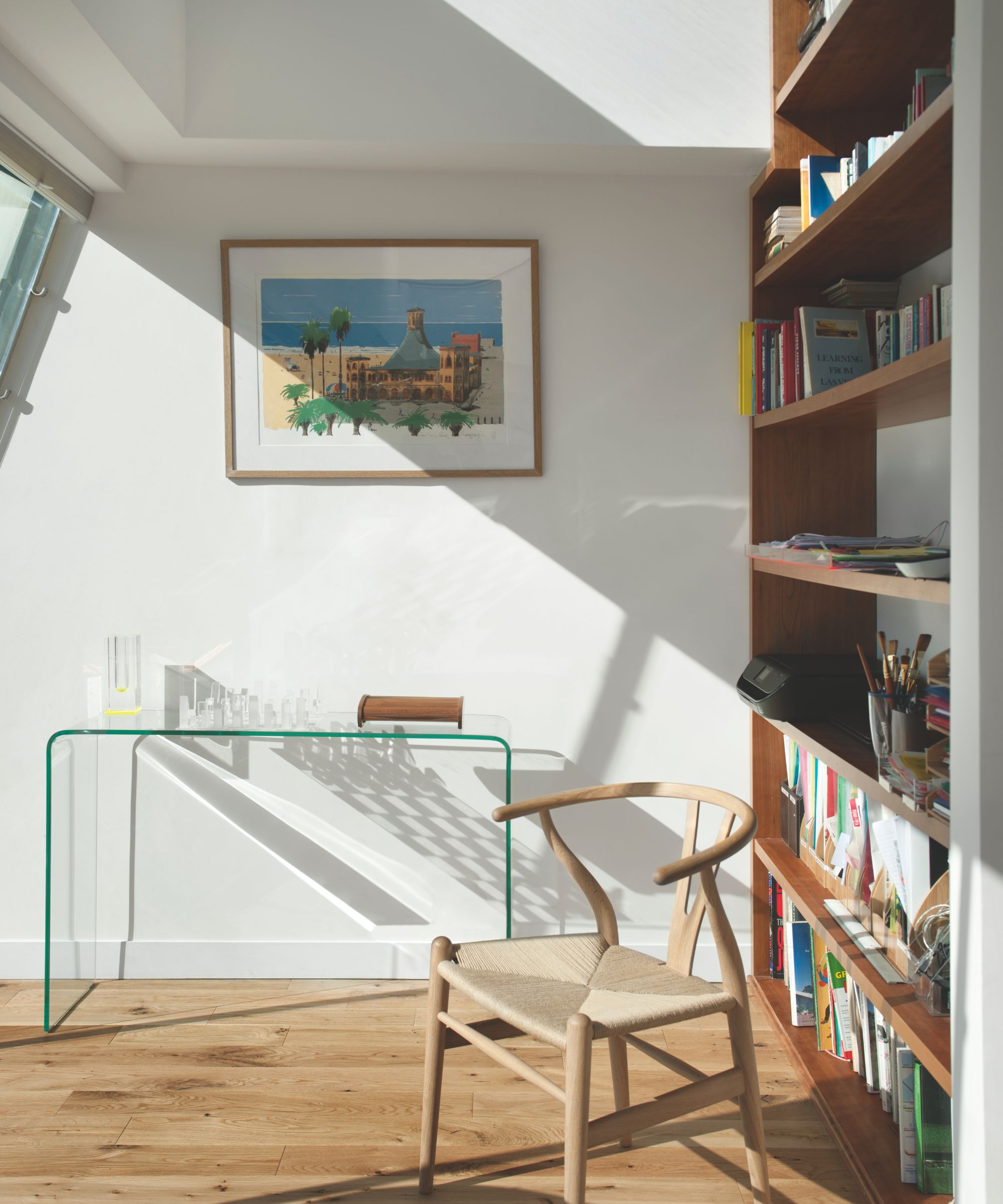 Midcentury modern style hallway with skylight, glass desk, curved wood chair, wood bookcase and framed painting