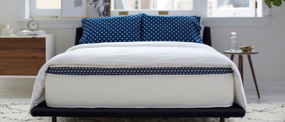 The WinkBed Mattress placed against a window in a light an airy bedroom. On top of the bed is a white comforter and two pillows