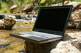An old laptop turned off resting on a rock by a stream