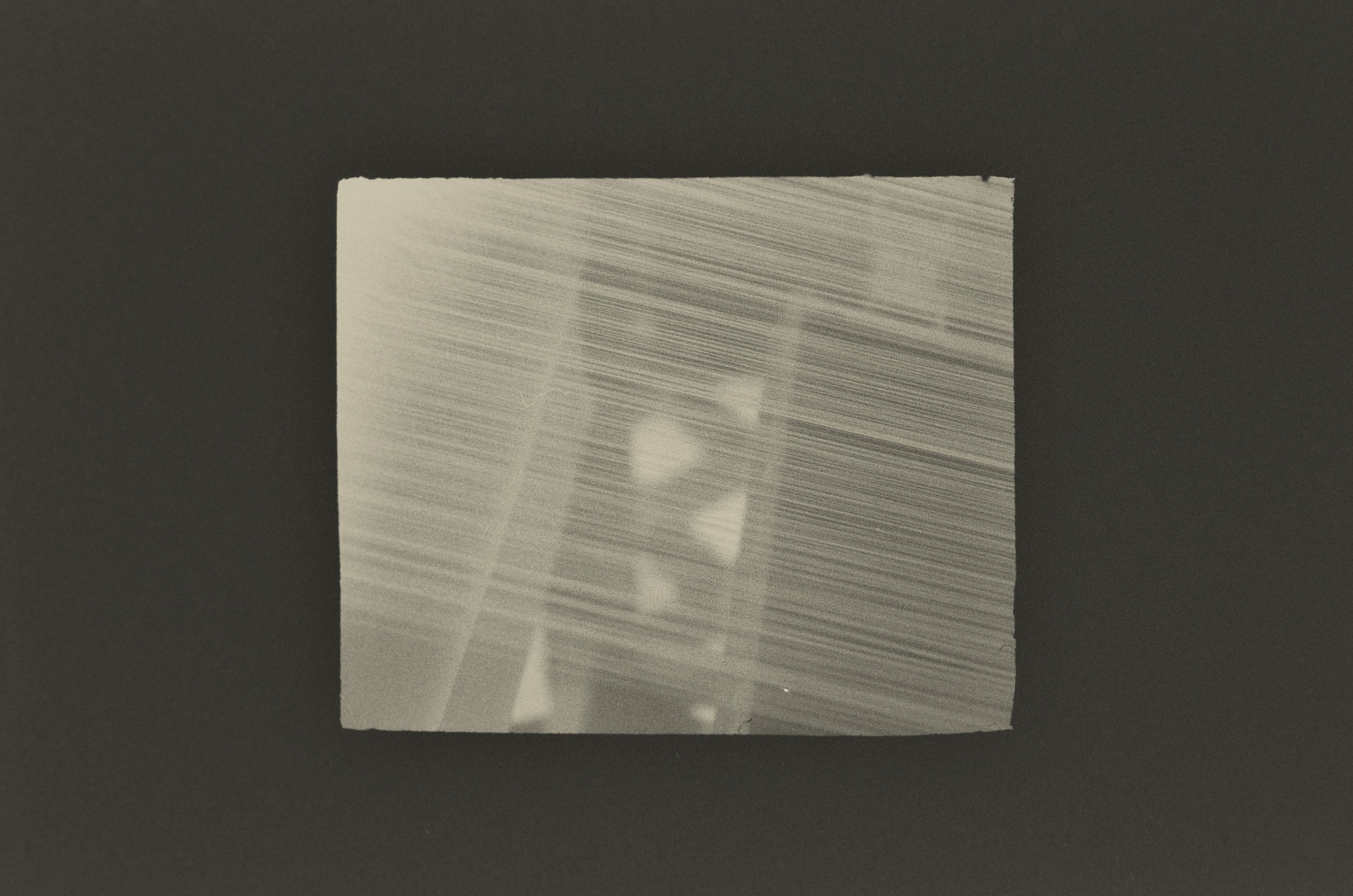 A black-and-white print by Jing Huang of silk threads streaking diagonally across the frame, with blurred bright shapes glowing through from behind.