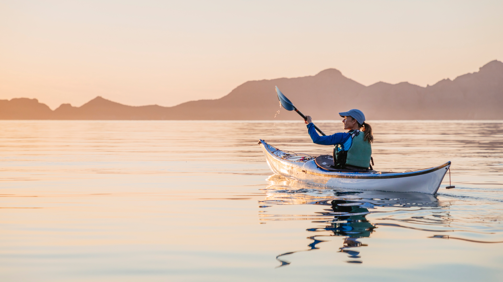 A woman kayaking in the sea at sunset