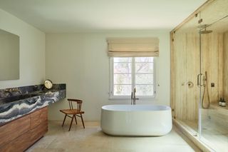 minimalist bathroom with freestanding bathtub, stone-clad shower, blinds and black stone counter with wooden cabinets