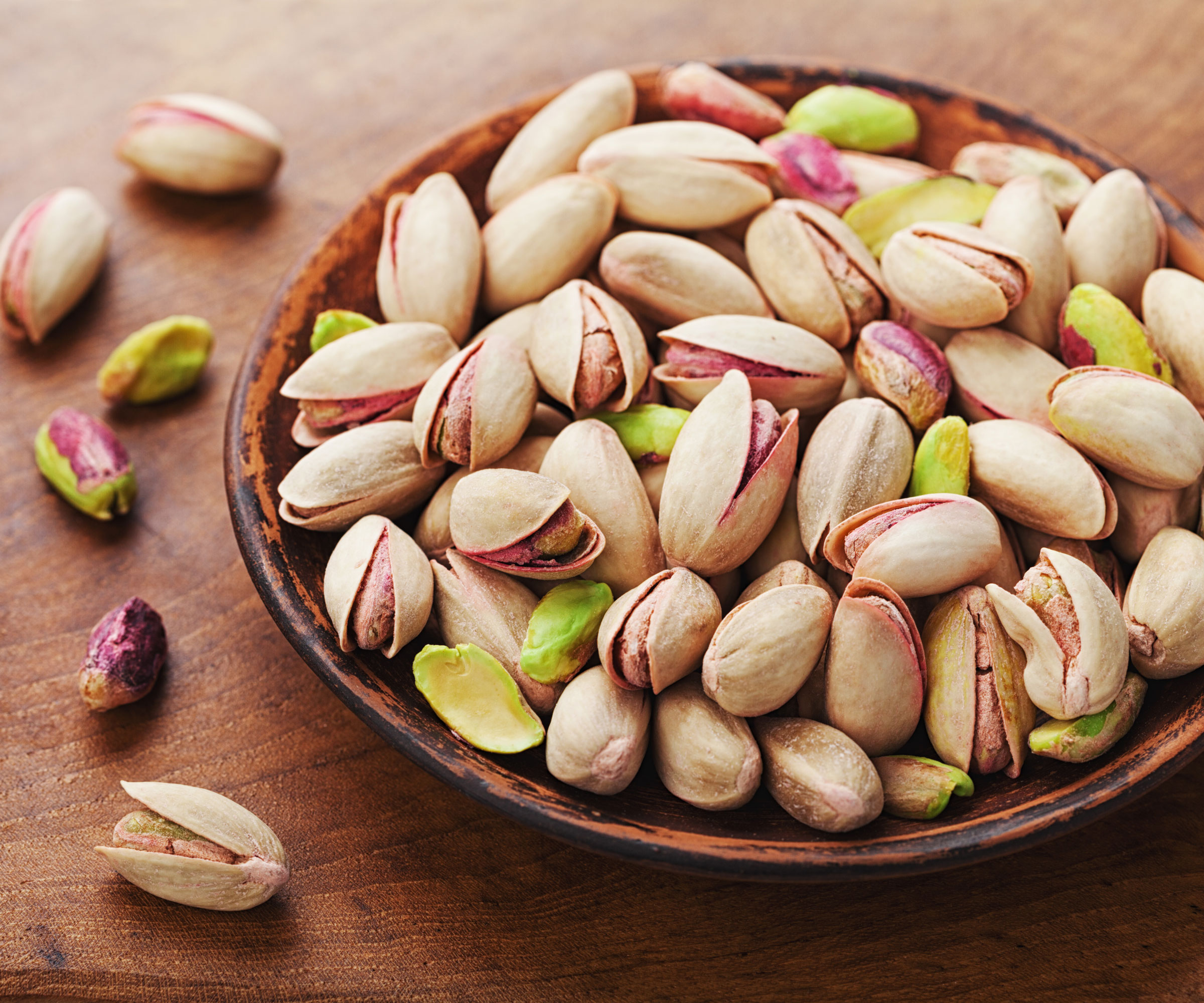pistachio nuts in shells in dish on wooden table