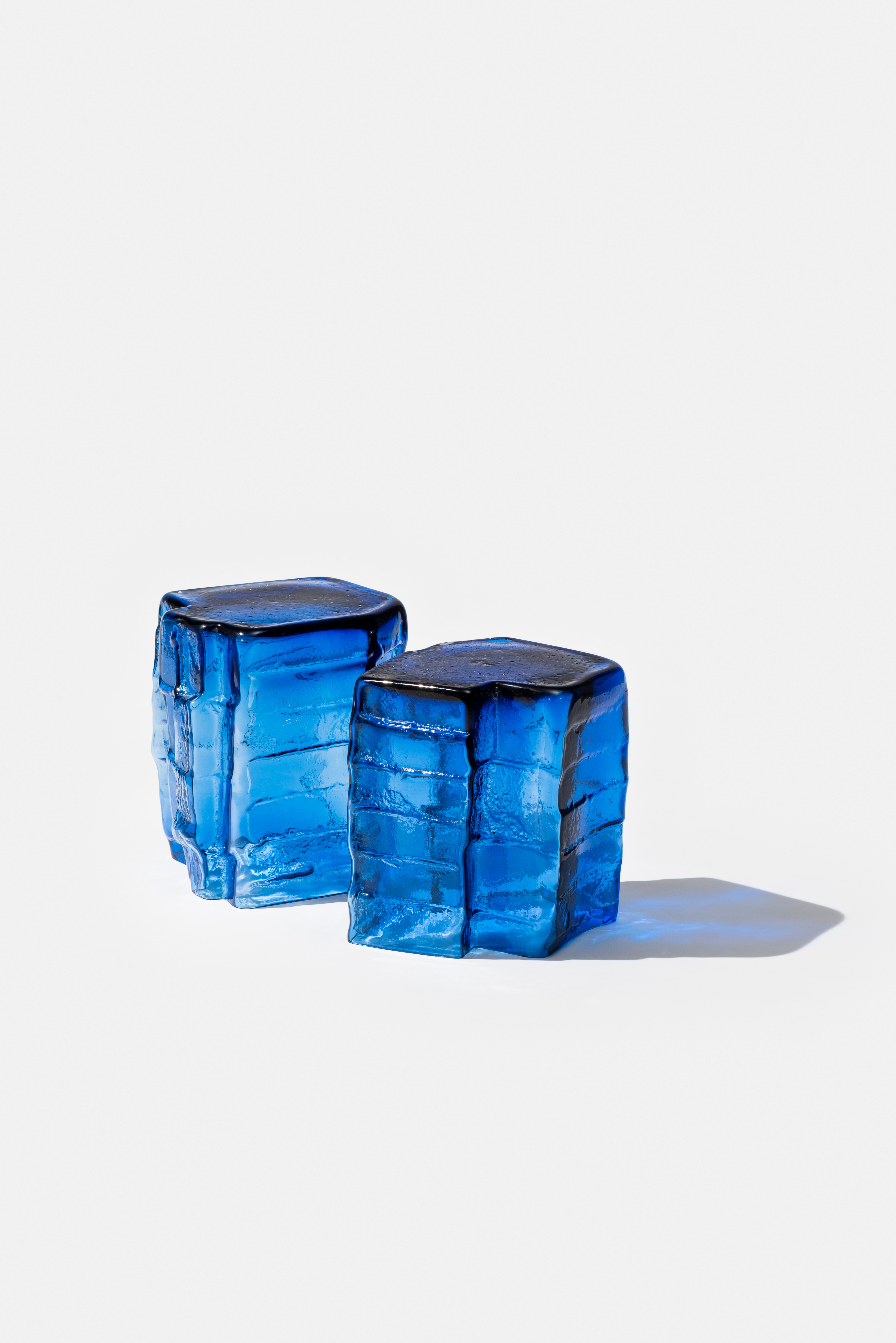 two blue cast glass sculptures in white background