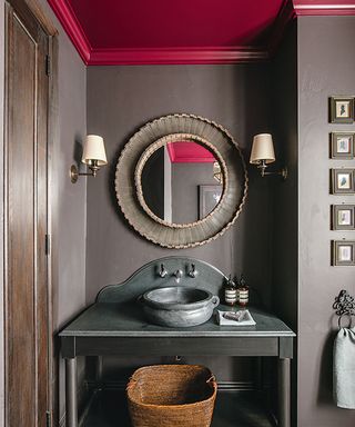 Bathroom with dark grey walls and vanity unit, round mirror and a plum colored decorated ceiling.
