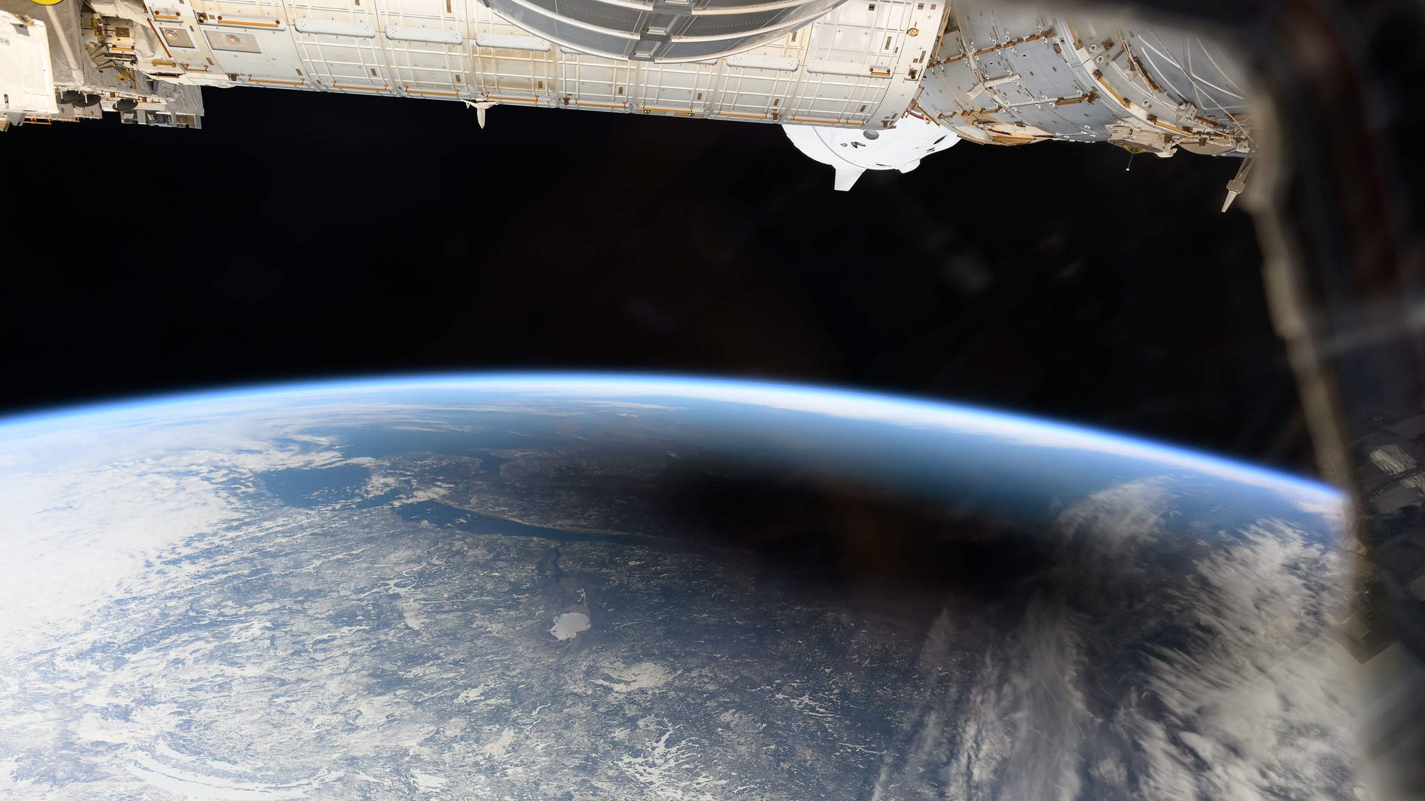 the earth with a black shadow over it. the international space station's modules are visible just above