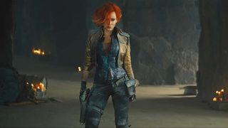 a woman (cate blanchett) with bright red hair stands in a cave with small fires in the background