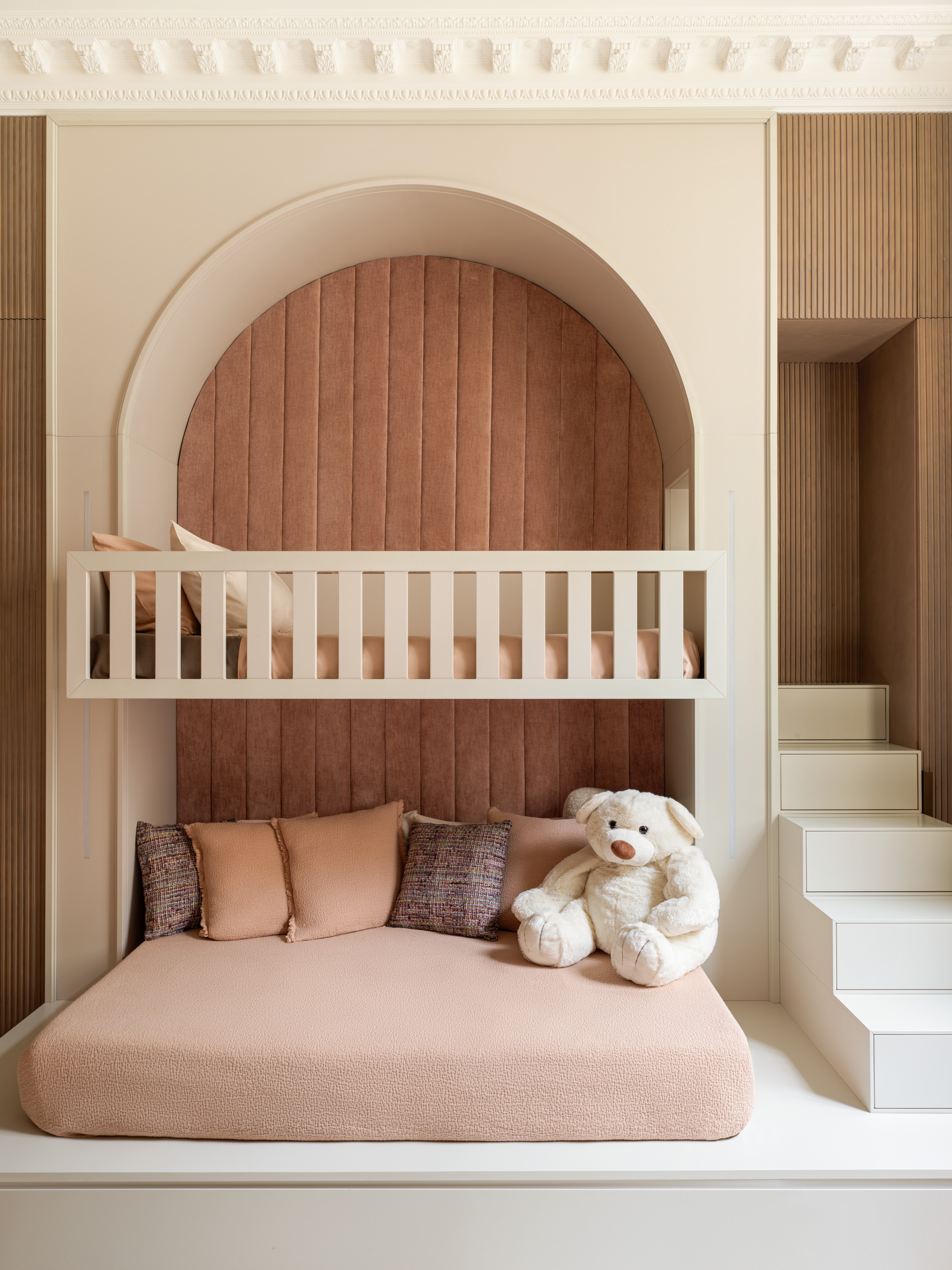 A pink and beige-themed child's room with a bunk bed-style set up – bed up top and daybed underneath, with stairs built in