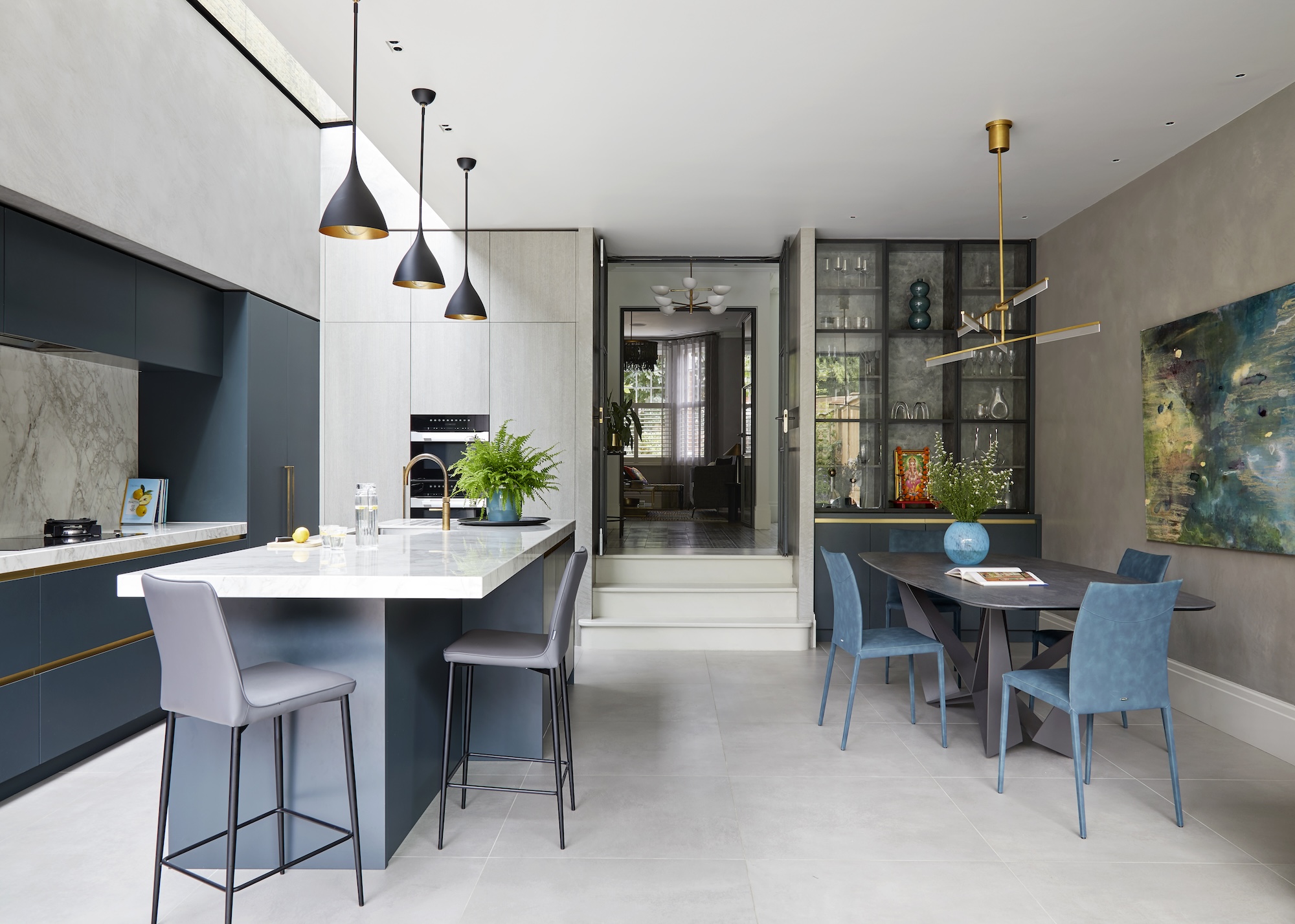 A kitchen with a dining area and an island with seating too. There is also a view of a floor to ceiling glass fronted cabinet.
