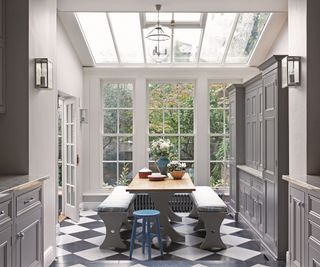 View from the kitchen to the glass roofed dining area, dark grey cupboards and black and white tiled floor.