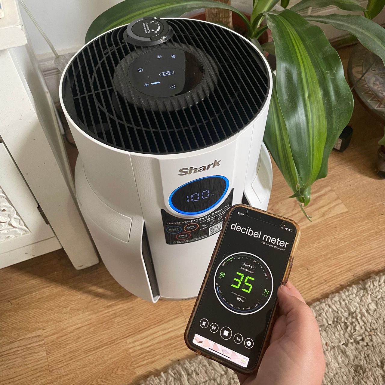 Hand holding a phone with a decibel meter on it in front of the Shark NeverChange 5 Air Purifier