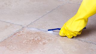 Cleaning grout on floor tile with toothbrush