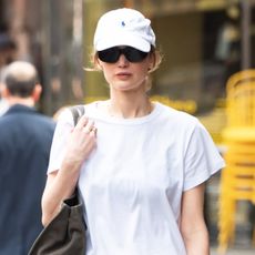 Jennifer Lawrence wearing a white T-shirt, black pull-on pants, black flats, and a Polo Ralph Lauren baseball cap