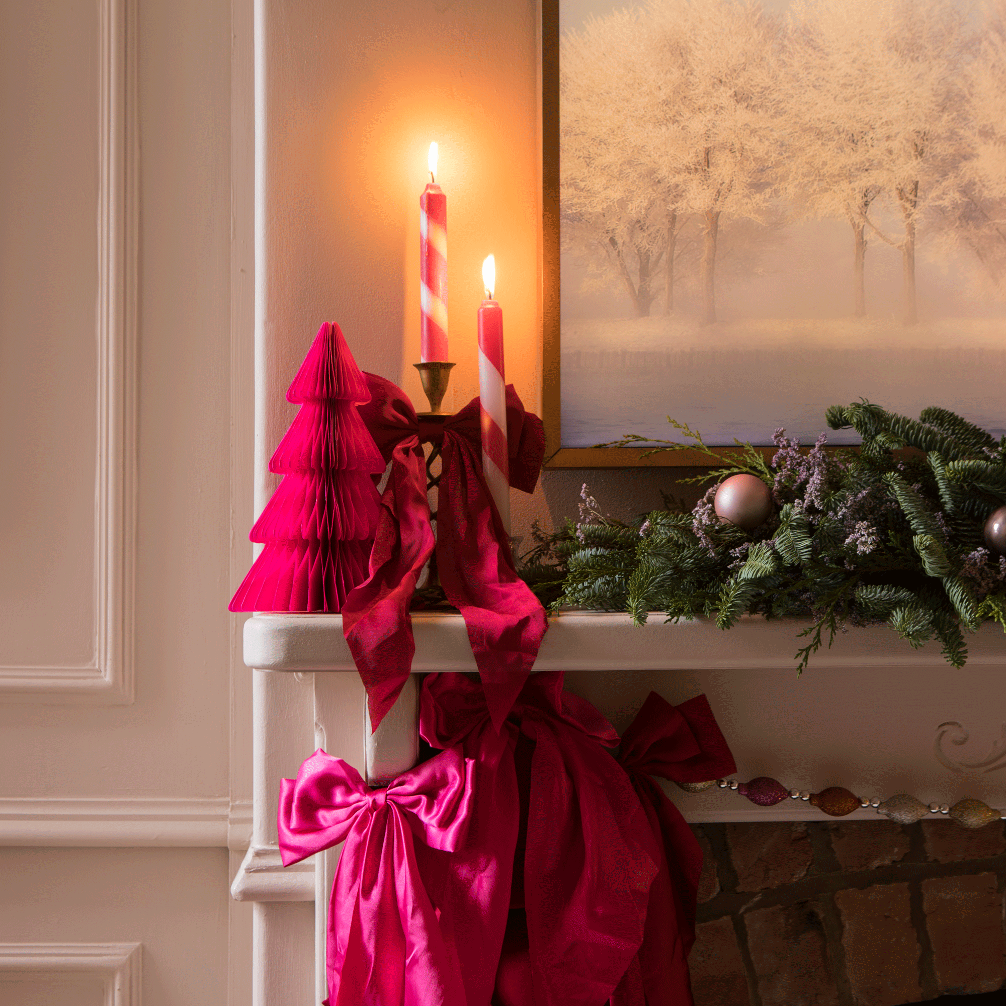 a living room mantelpiece with festive greenery, candles, a bold pink paper Christmas tree and plenty of bows
