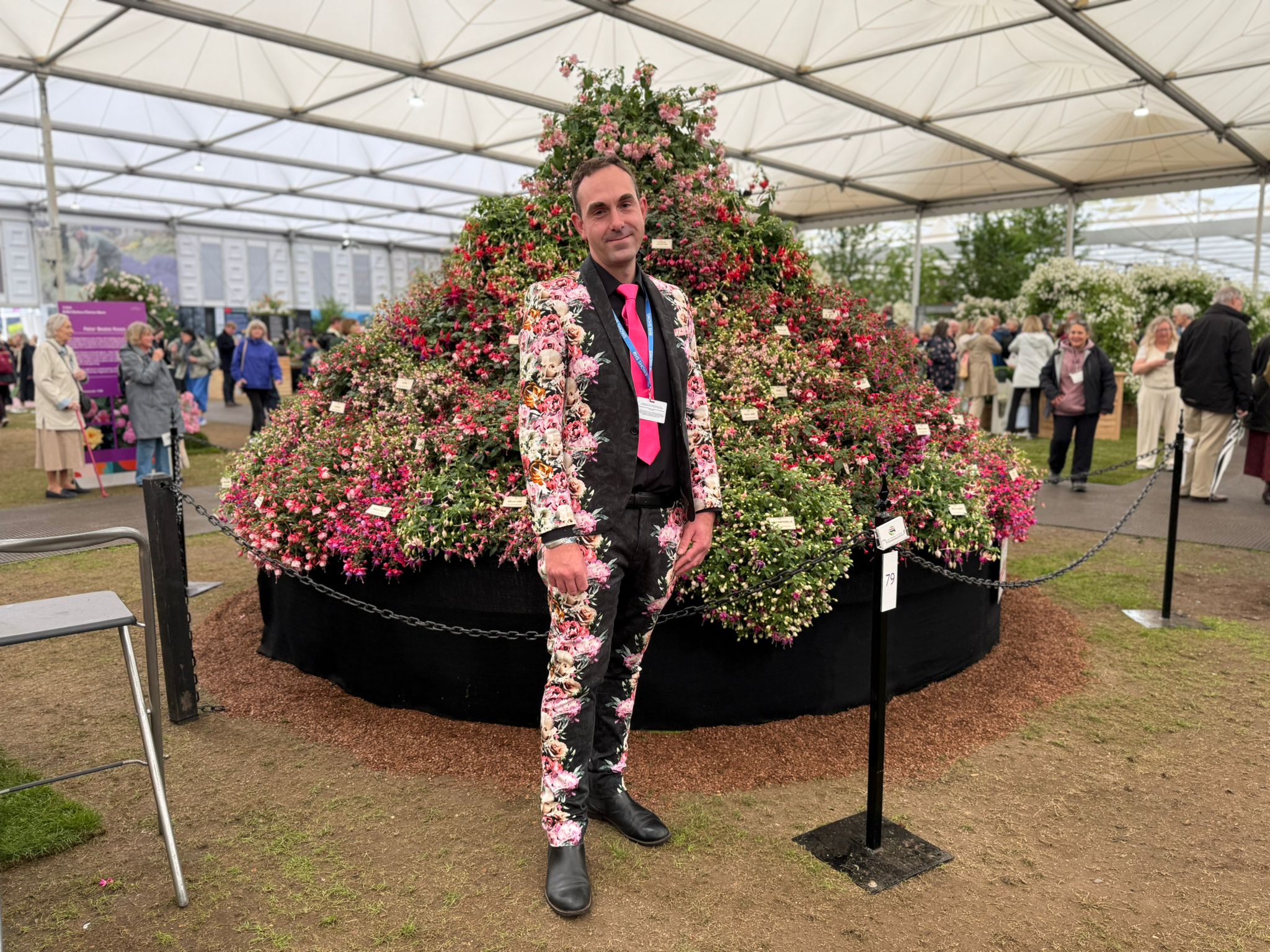 A man in a colourful suit stands in front of a searing Fuchsia display