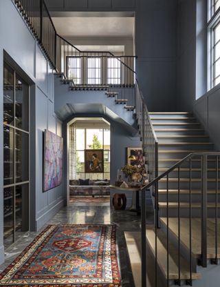 Hallway with rug on floor and staircase and view to living room with blue paint on walls