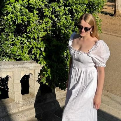 Flora Vesterberg wearing a white dress walking up a staircase with a tree in the background