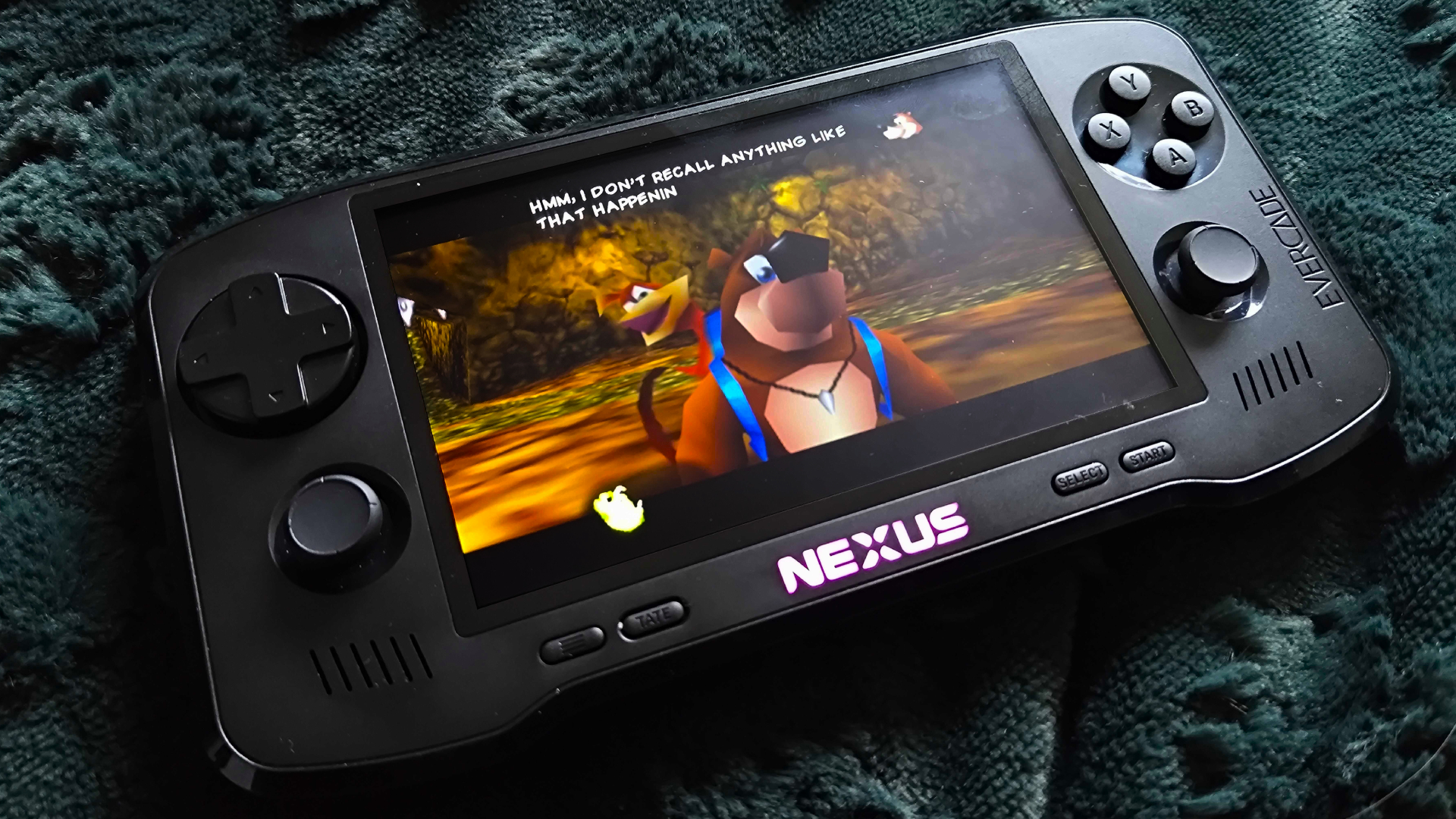 Evercade Nexus handheld on green throw with Banjo-Tooie cutscene on screen with Banjo saying &amp;quot;Hmm, I don't recall anything like that happenin&amp;quot;