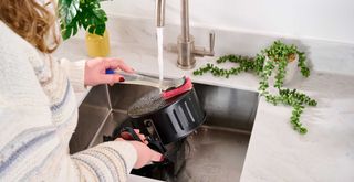 Person cleaning an air fyer basket with washing up liquid over a sink