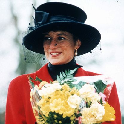 Princess Diana wearing a red coat and black hat holding flowers