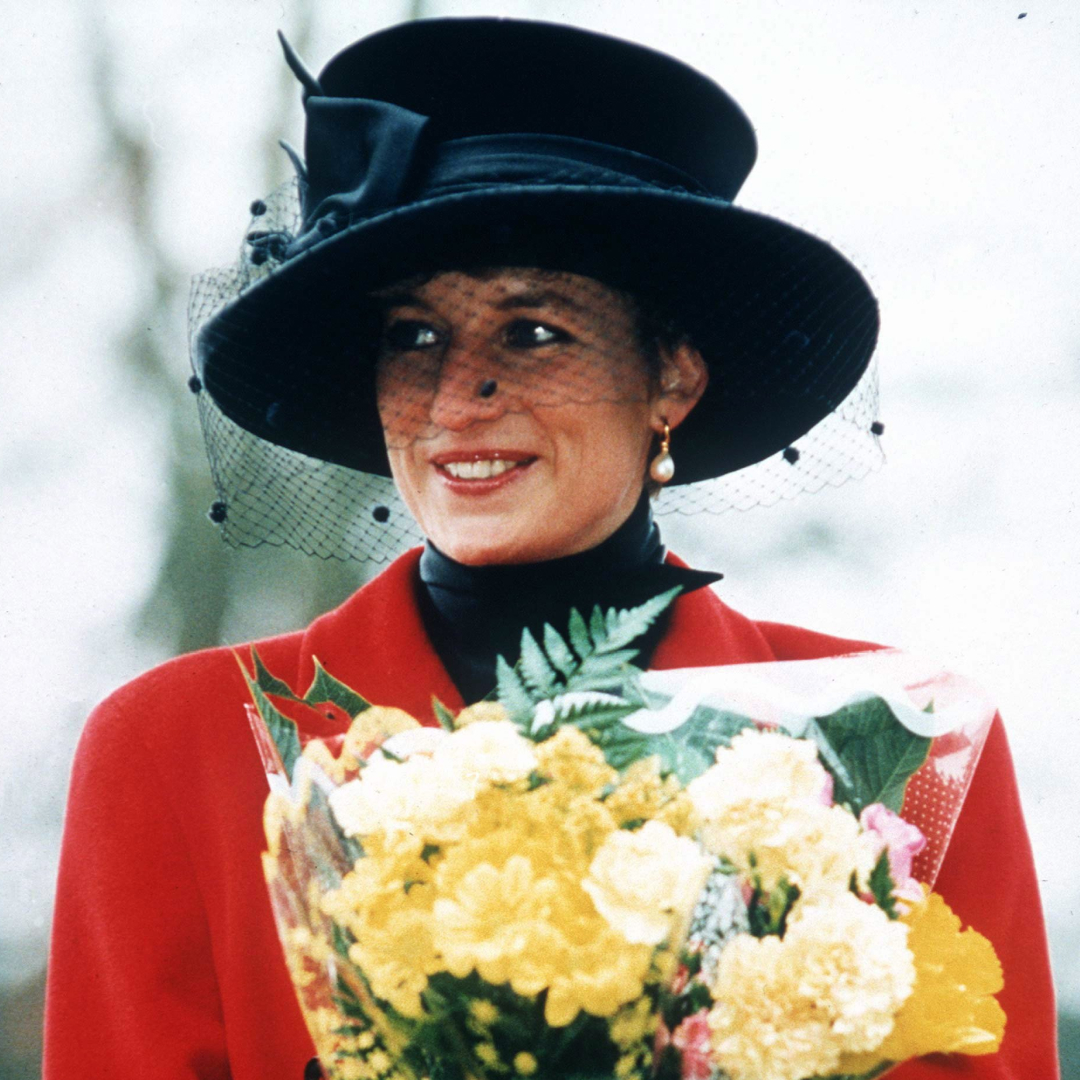 Princess Diana wearing a red coat and black hat holding flowers
