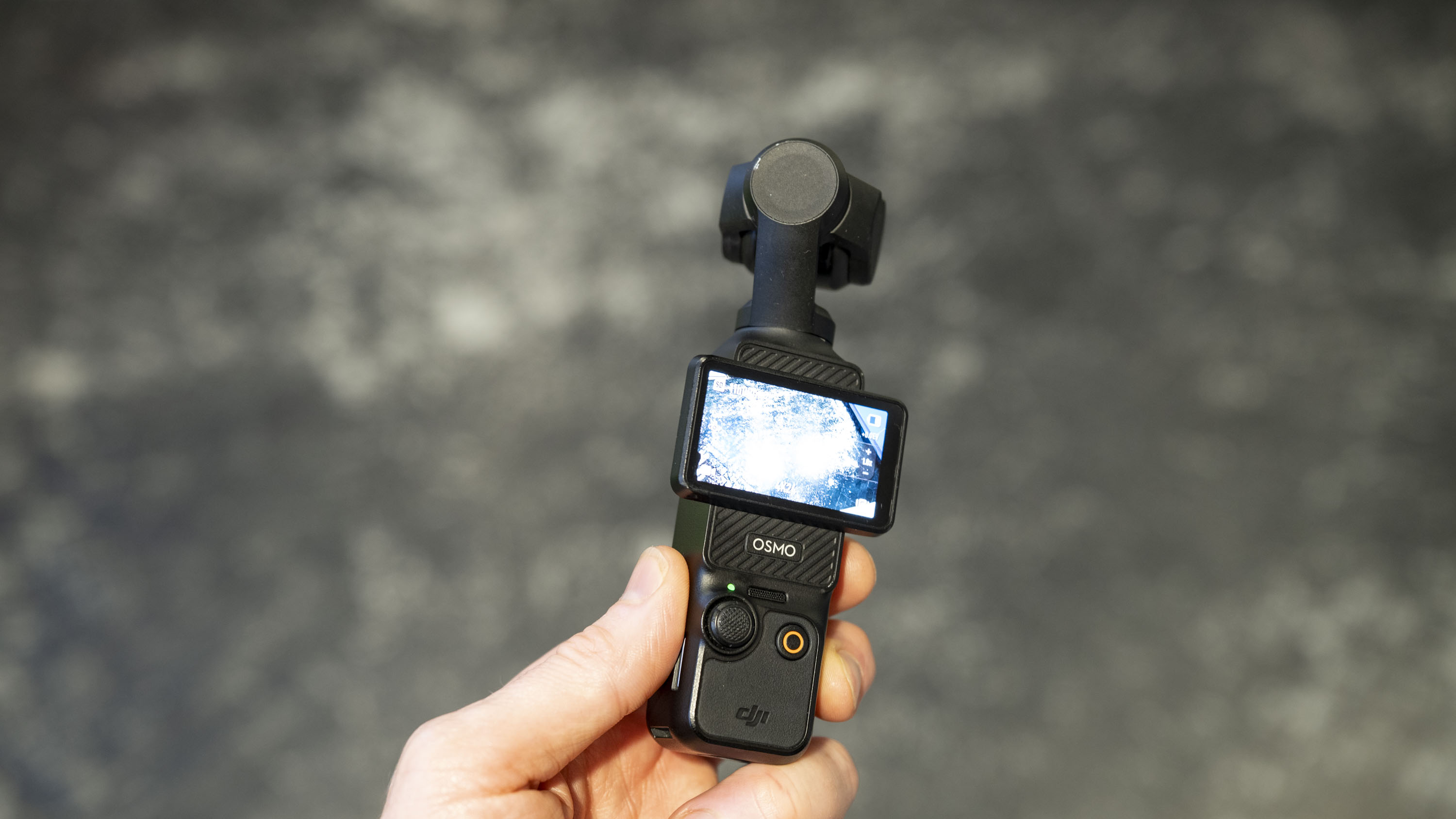 DJI Osmo Pocket 3 vlogging camera in user's hand, grey floor in background