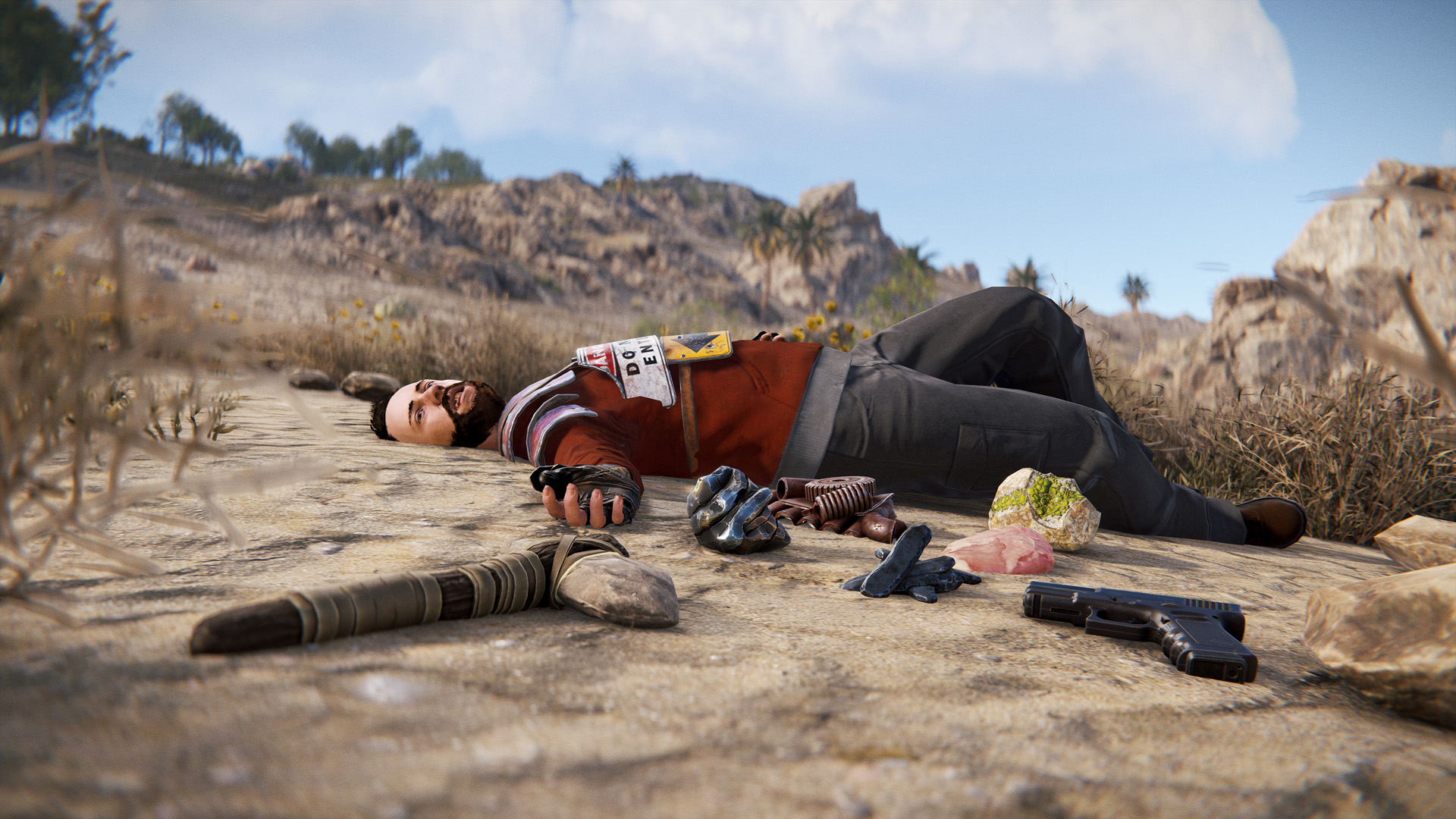 A player lies dead in the sand, surrounded by weapons and equipment in Rust.