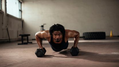 A man performing push-ups on a pair of dumbbells as part of a full-body muscle-building workout 