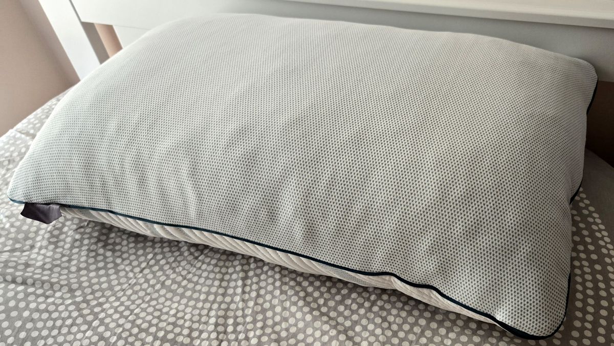 The back side of the Tempur-Pedic Tempur-Adjust ProAdjust Pillow, featuring a netted design, on top of a bed with a grey and white comforter