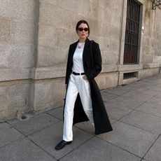 Annabel wears a white top, white jeans, black flats, and a black coat.