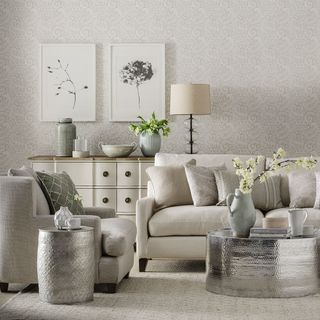 patterned wall living room with wall-mounted picture frames above a wooden-top chest drawer with accessories, and grey-creamed colored sofas with metal tables