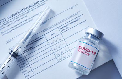 A vial of coronavirus vaccine on a vaccination record card with a syringe on the side