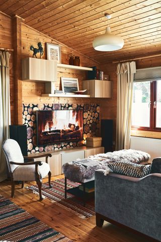 A cosy living space with fake log backdrop, sheepskin-covered footstool and second-hand furniture