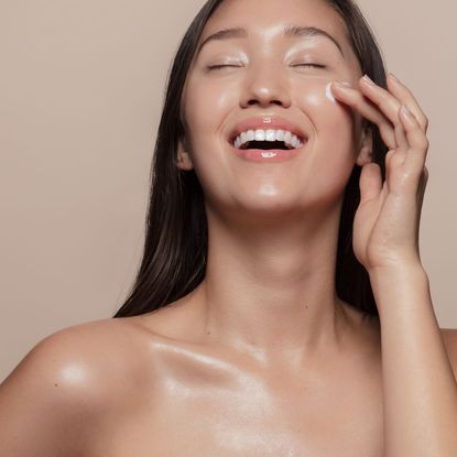 smiling woman with really glowy skin applying face cream - getty images 1142851205