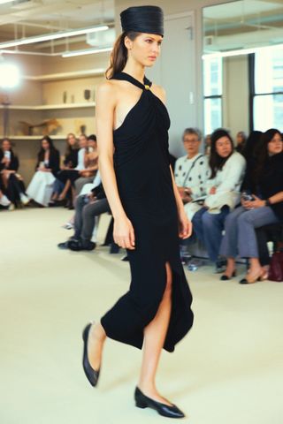 An Altuzarra model wearing a pillbox hat with a black dress and flats at the FW24 show.
