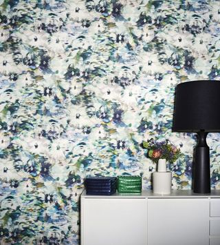 White cupboard with lamp on top in front of colorful floral Wallpaper