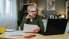 An older man works on his laptop while financial planning at his kitchen table.