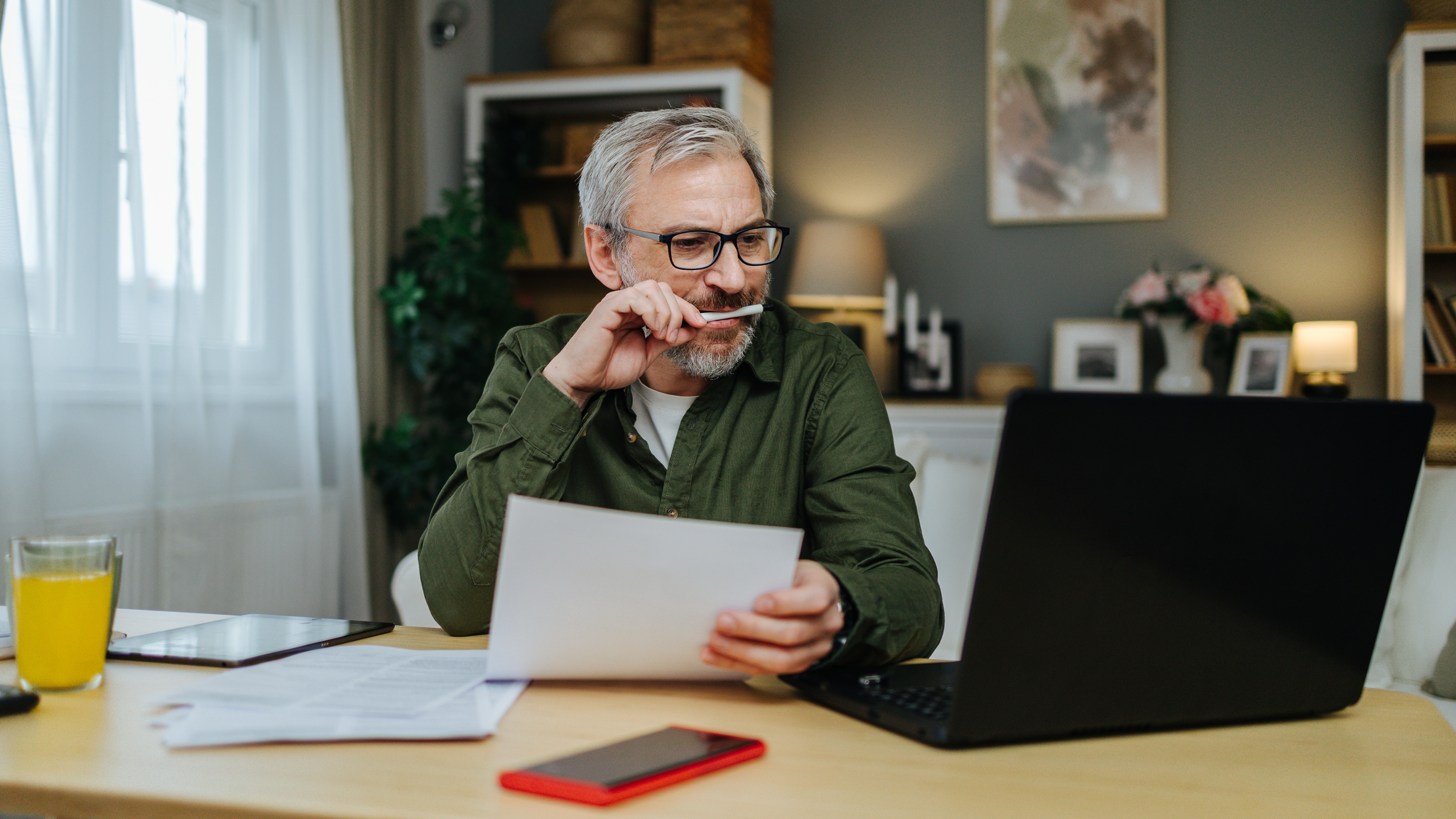 An older man works on his laptop while financial planning at his kitchen table.
