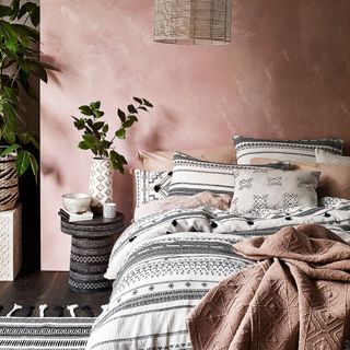 bedroom with pink wall bed with cushions wooden flooring and plant