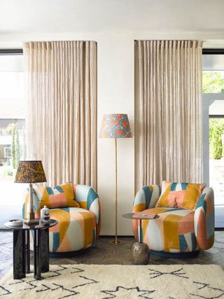 living room with matching armchairs with bold print fabric, patterned rug, black side table, drapes, floor lamp with patterned shade, table lamp with patterned shade