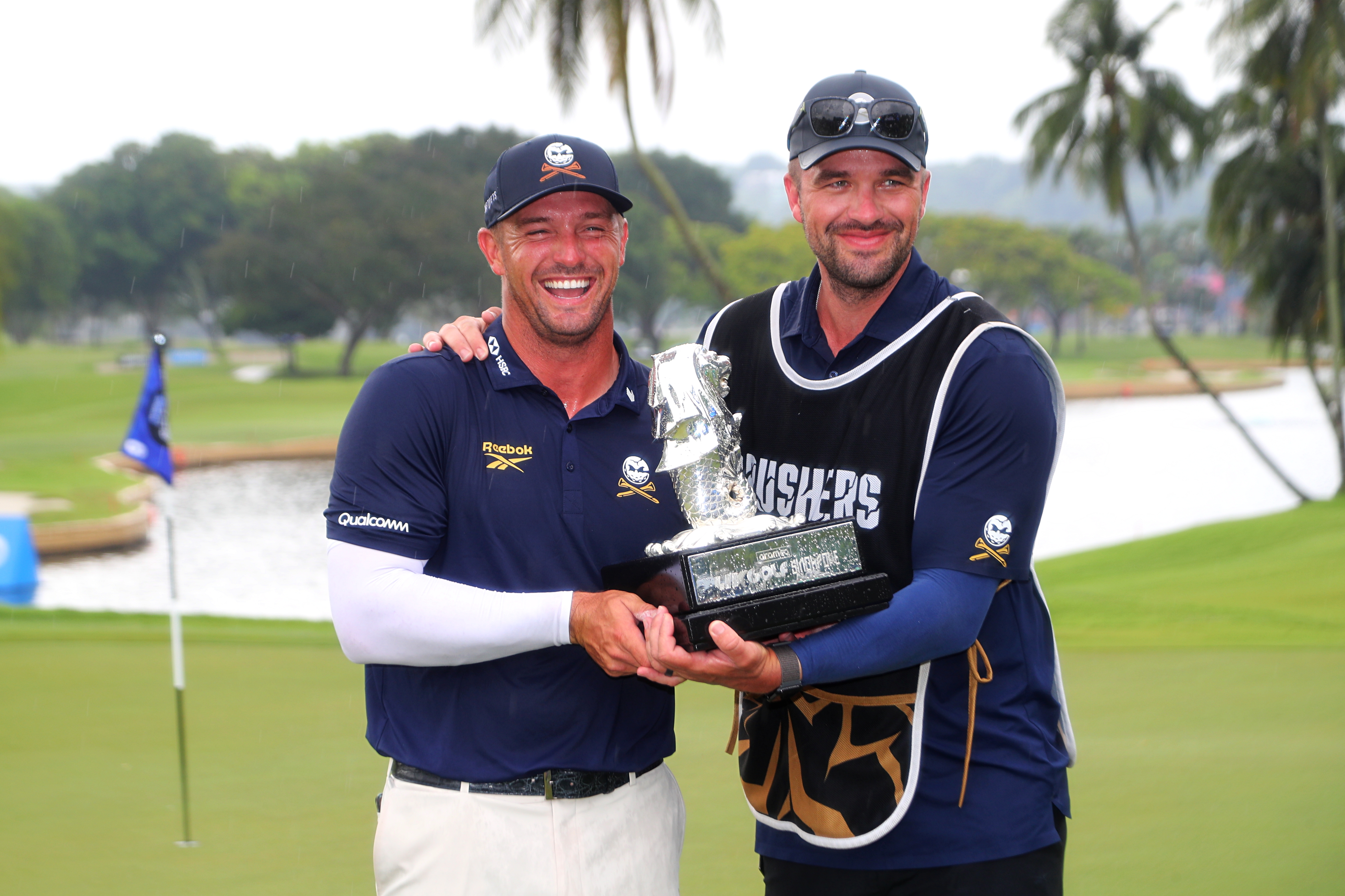 Bryson DeChambeau and his caddie pose with a trophy