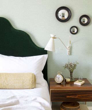 A bedroom color idea with green and white wallpaper and dark green velvet headboard