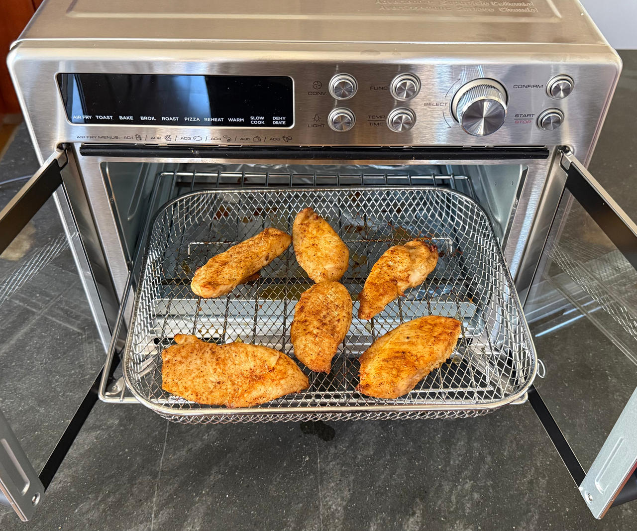 Breaded chicken pieces on a wire baking tray inside a two door stainless steel air fryer oven.